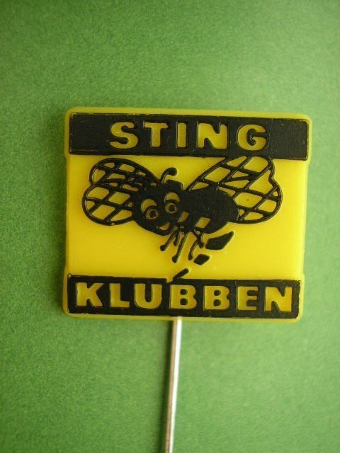 Gul och svart pin med bi, texten "STING KLUBBEN", mot grön bakgrund.