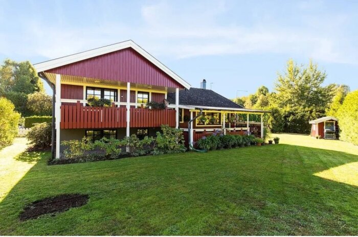 Rött hus med veranda, grönskande trädgård, gräsmatta, soligt, fridfullt bostadsområde.