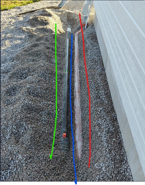 Grusväg mot husvägg, rör och kabel markerade med färglinjer för identifiering, installation pågår.