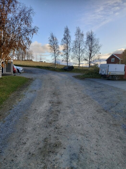 Lantlig väg, träd, himmel, fordon, byggnad, grusväg, höstfärger, öppet landskap, delvis molnigt.