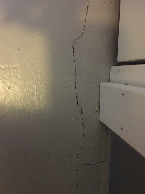 En spricka i en grå vägg vid ett hörn intill vit trappa. Möjlig strukturproblem eller slitage.