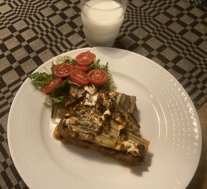 Portion lasagne med sallad och tomat, glas mjölk, rutig bordstablett.