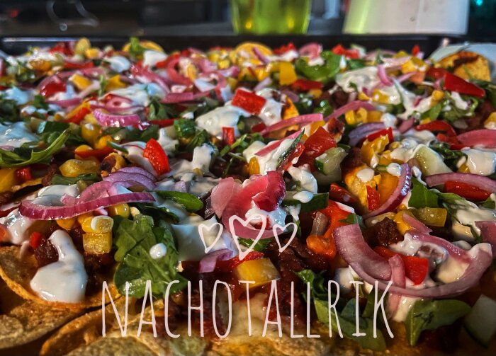 Nacho tallrik med färgglada grönsaker, rödlök, dressing, och texten "NACHOTALLRIK" överlagrat på bilden.