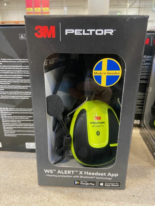 Förpackning med 3M Peltor hörselskydd, Bluetooth, grön, "Made in Sweden" klistermärke, appkompatibel, står på en hylla.