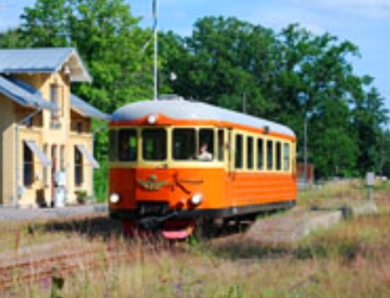 Gammal orange tågvagn vid en övergiven järnvägsstation, soligt, grönt gräs, delvis oskarp bild.