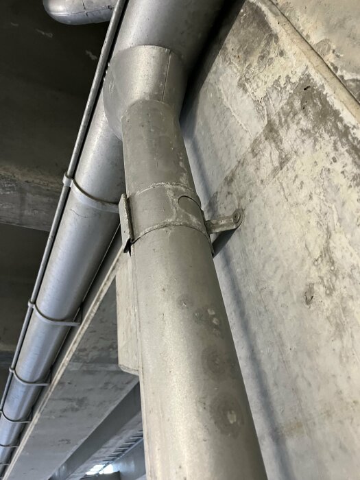 Metalliska rör på en betongvägg i underjordisk miljö – installation för ventilation eller vattenavlopp.