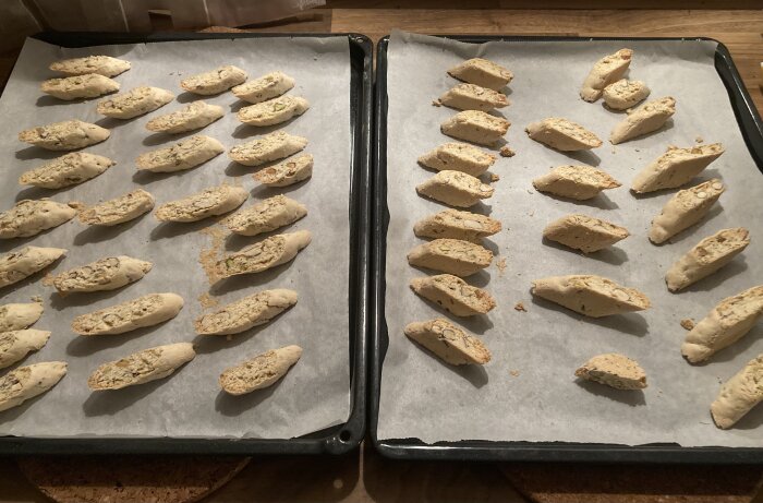 Två plåtar med hemlagade biscotti på bakplåtspapper, redo för andra bakningen.