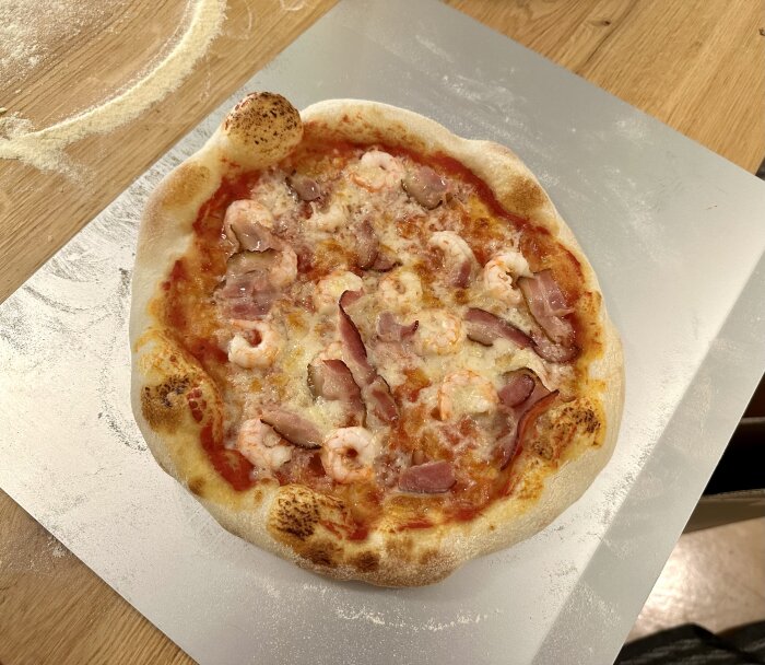 Nybakad pizza med skaldjur och skinka på skärbräda, mjölströdd träbänk, hembakat utseende.