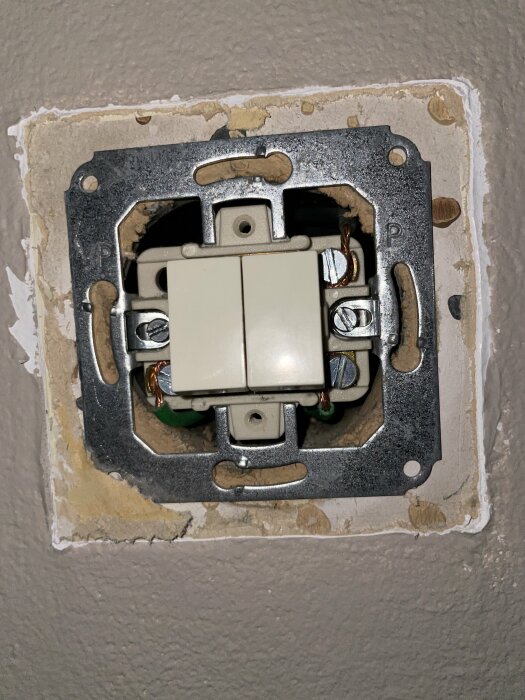 Eluttag utan skyddsplatta, synliga ledningar, skruvar, installationsarbete, betongvägg, behöver åtgärdas.