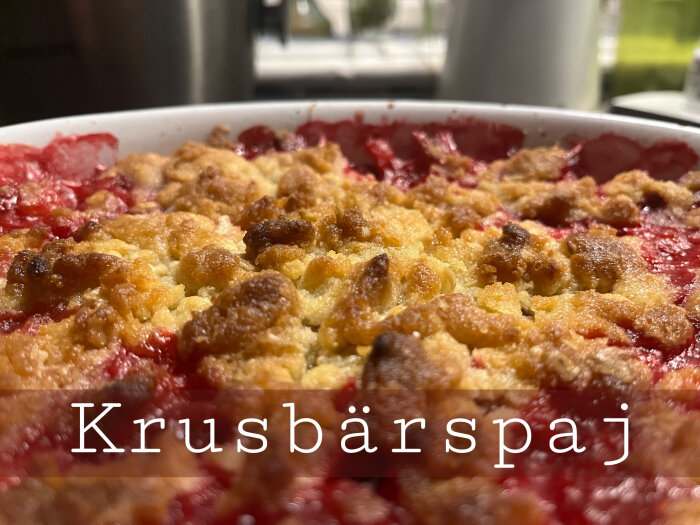 En nybakad krusbärspaj med gyllenbrun smuldeg, röda bär synliga, text "Krusbärspaj" framför, hemlagad dessert.