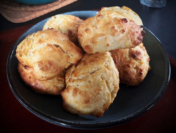 Nybakade, gyllene scones på svart tallrik, rustik hemmabakning, morgonfika atmosfär.