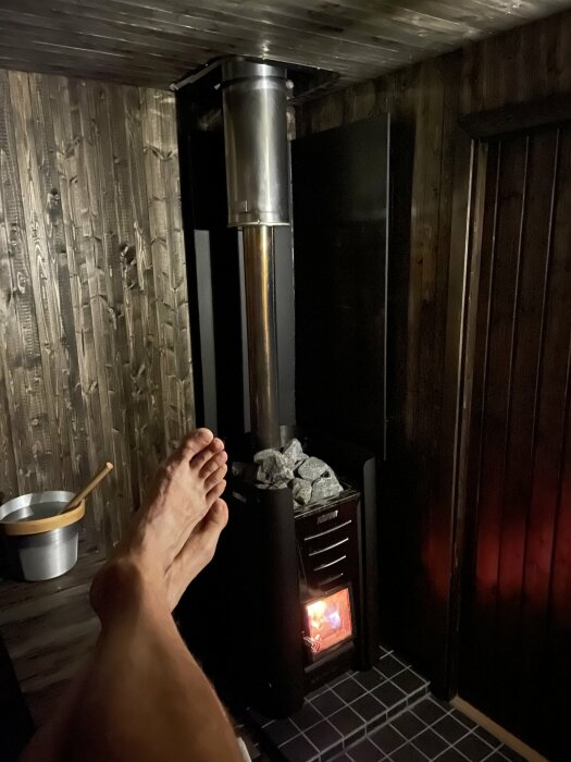 Avkoppling i bastu med synliga fötter, eldstad, glödande stenar, värme, träväggar.