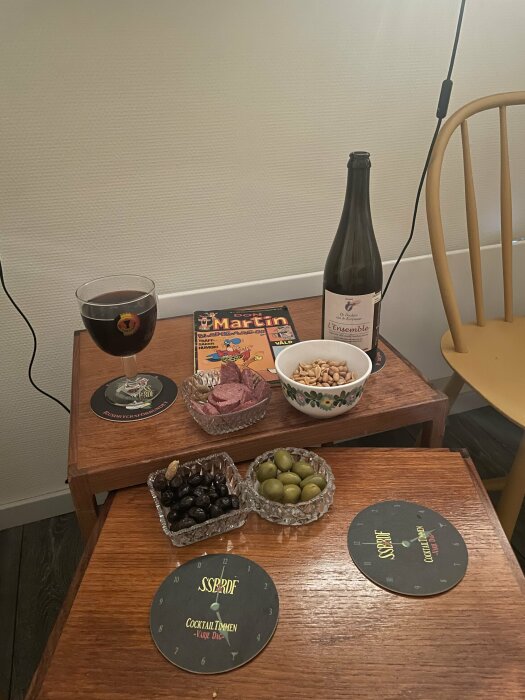 Ett bord med vin, snacks, glas, serietidning och underlägg. Inbjuder till en avkopplande stund.