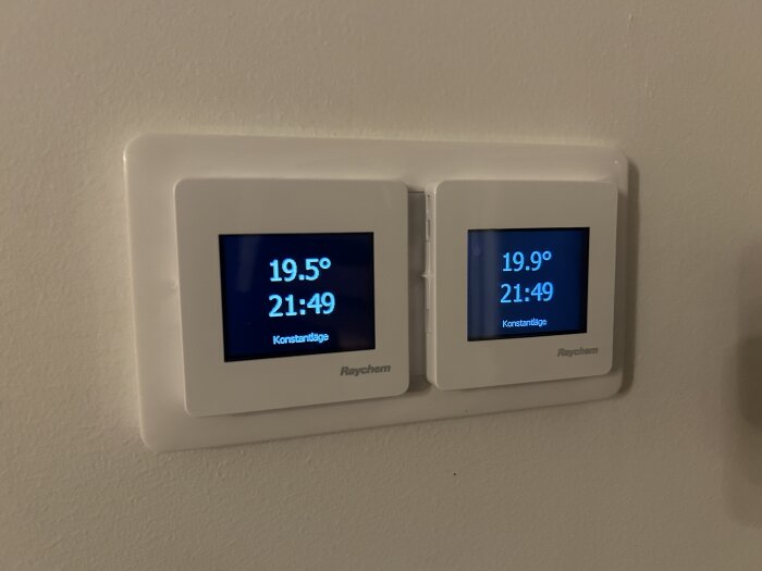 Två digitala termostater visar temperatur och tid på en vägg.