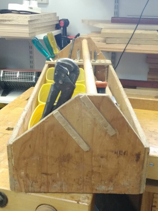 Verkstadsverktyg i en träredskapslåda, inklusive skruvmejslar och tänger, på en arbetsbänk.