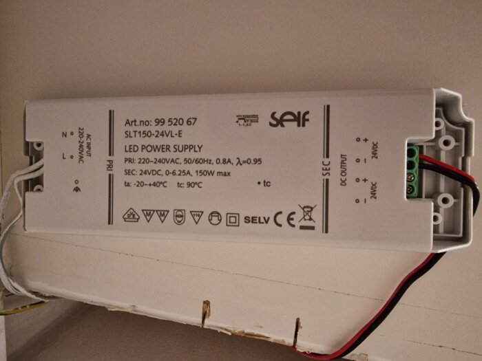 LED-strömförsörjning monterad på vit yta, elledningar anslutna, tekniska specifikationer synliga.