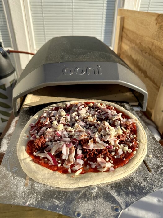 Ooni pizzaugn med outgräddad pizza, toppad med tomat, ost, lök, kött.
