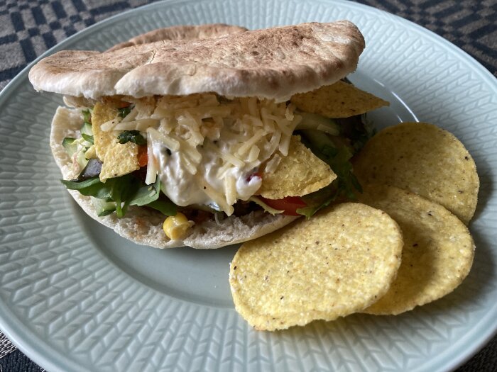 Pita brödsandwich med sallad, ost och majskex på en tallrik.