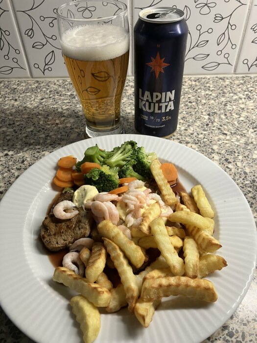Middagstallrik med kött, räkor, pommes frites, grönsaker, ölburk och glas på köksbänk.