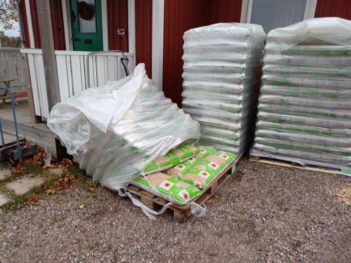 Byggmaterial av isolering på pallar täckta med plast utanför en byggnad. Höstblad på marken.