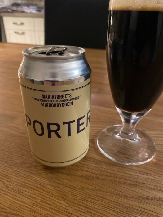 Öppnad burk porter, Mariatorgets Mikrobryggeri, bredvid fyllt ölglas på träbord.