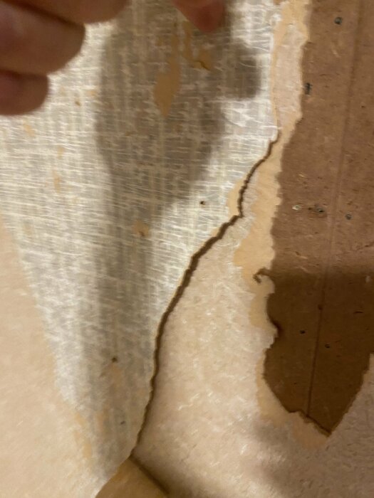 Närbild på hand som drar tapet från vägg, avslöjande underliggande lager och strukturer.