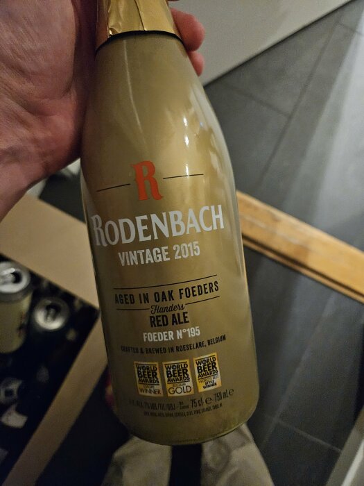 Hand håller Rodenbach Vintage 2015 flaska, gyllene kåpa, flamländsk rödöl, ekfatslagrad, belgisk, världsmästare.