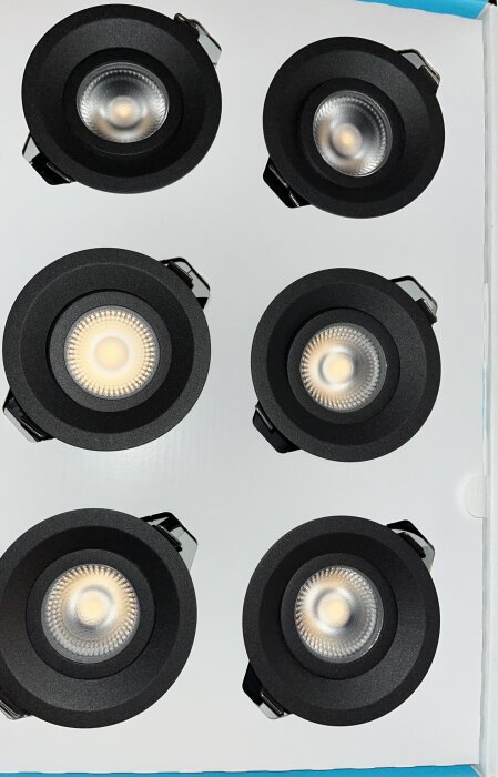 Sex svarta runda infällda LED-lampor i kartong, fyra tända, uppifrån vy.