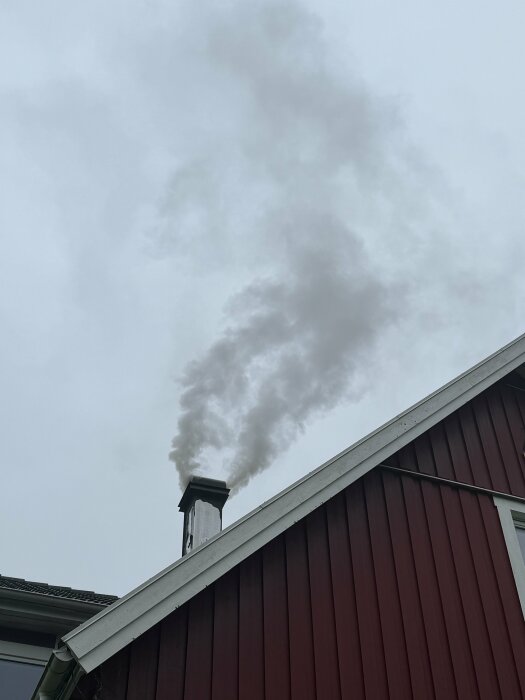 Röd byggnad, skorsten, tjock rök, molnig himmel.