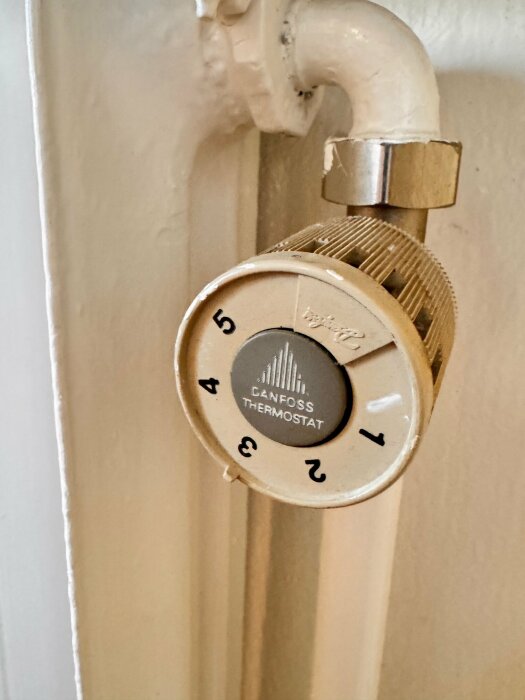 Termostatventil på radiator, märkt "Danfoss Thermostat," numrerad skala 1 till 5, vit bakgrund, rördragning ovanför.