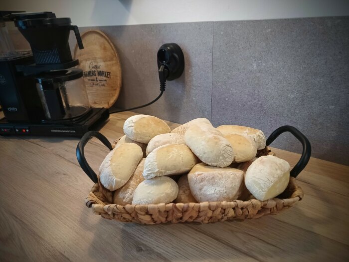 Korg med bröd på köksbänk, kaffebryggare, träskärbräda och vägguttag i bakgrunden.