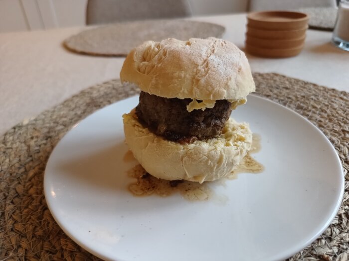 En hemlagad hamburgare på tallrik med bröd, köttbiff och ost, serverat på köksbord.