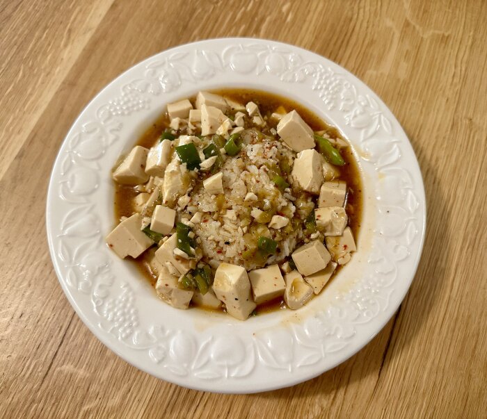 Vitt tallrik med tofu, salladslök, kryddor, kanske asiatisk maträtt, på ett träbord.