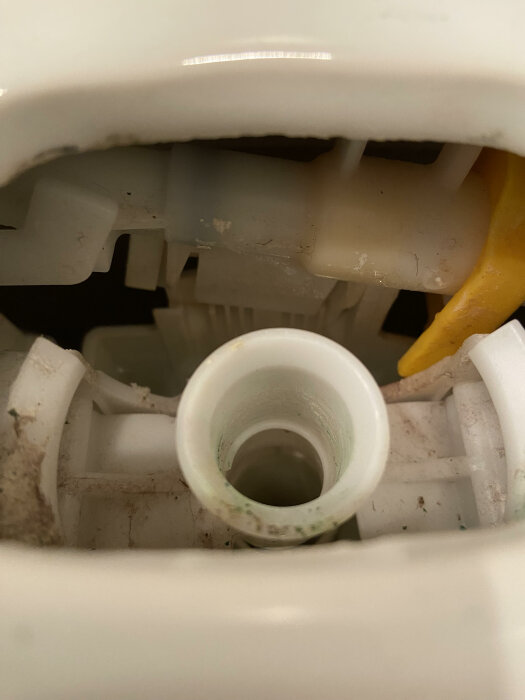 Inuti en toalettcistern, vita plastdetaljer, vatteninloppsrör, behöver rengöring, synlig smuts och kalkavlagringar.