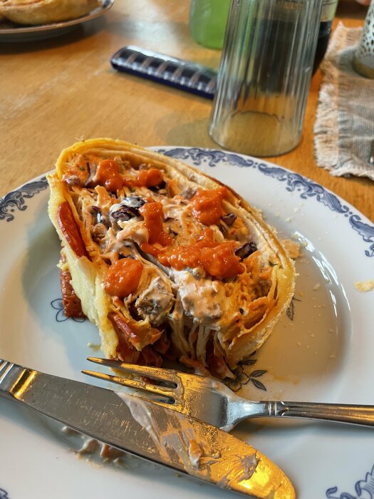 En uppskuren paj på tallrik med redskap, möjligtvis fylld med kyckling och grönsaker, ovanpå ett bord.