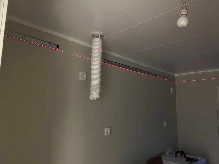 Inomhusrum med grå väggar, takventilation, rosa LED-list, ombyggnation pågår, glödlampa hänger från taket.