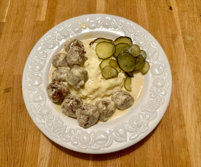 En tallrik med köttbullar, potatismos och inlagda gurkor serveras på ett träbord. Traditionell svensk maträtt.