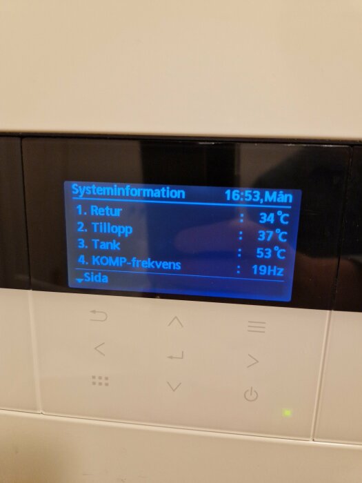 Digital display visar temperatur och frekvens för en värmesystemkomponent, med knappar för navigering nedanför.