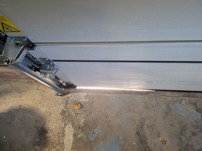 Garagedörröppnare med sensorer på en sliten betonggolv framför vit garageport.