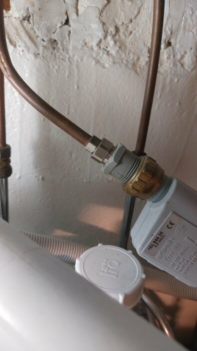 Kopparledning med kopplingsdetaljer och kablar på en vitmålad väggbakgrund, inomhus VVS-installation.