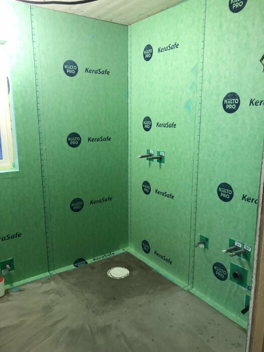 Ett ofärdigt badrum med gröna våtrumsskivor, VVS-installationer synliga, ej kaklat eller möblerat än.
