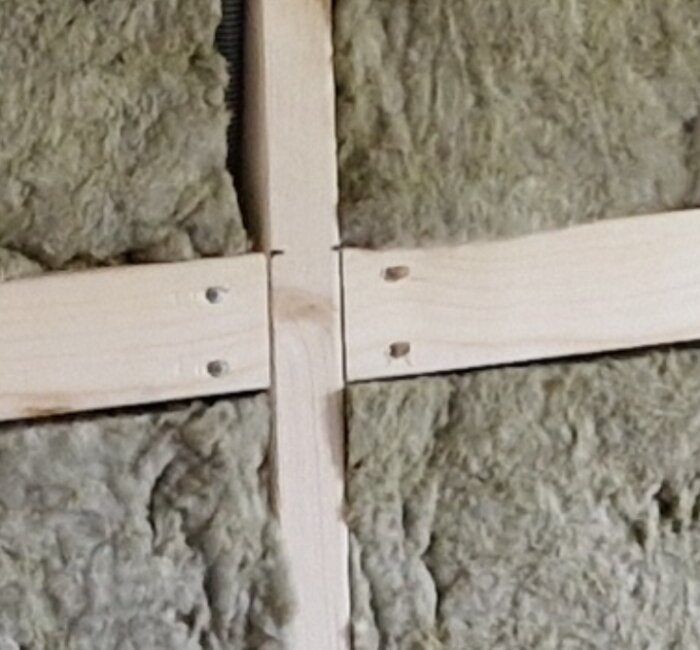 Träreglar monterade i kors över isoleringsmaterial, säkert för bygg- eller renoveringsarbete.
