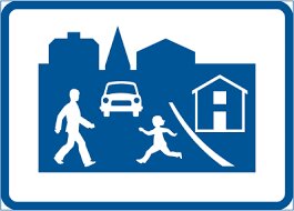 Blå och vit skylt: vuxen och barn går, bil, hus, stadssiluett, troligen varning för skolområde.