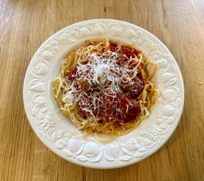 Spaghetti med köttbullar, tomatsås, riven ost på ett dekorerat vitt fat.