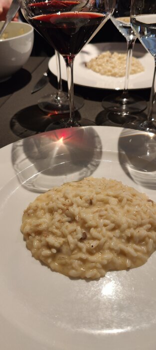 Portion av risotto på tallrik med rödvin och vattenglas i bakgrunden, inomhus, elegant måltid.