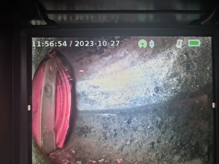Kamerafokus på skärmen, visar datum, tid, röd objekt, grön batteriindikator, suddig bakgrund.