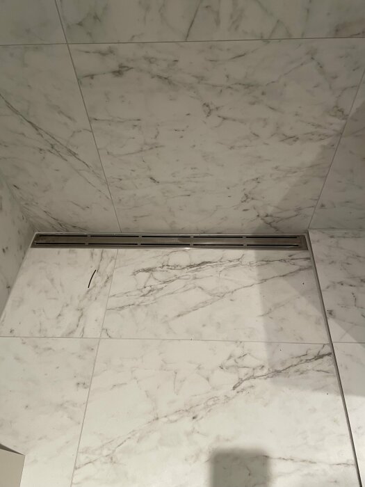 Marble-patterned tiles in a corner, shadow visible, modern minimalist design, with a linear shower drain.