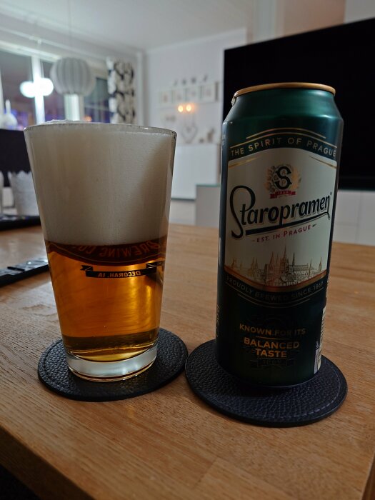 En ölburk Staropramen och ett glas öl på svarta underlägg i ett hem.