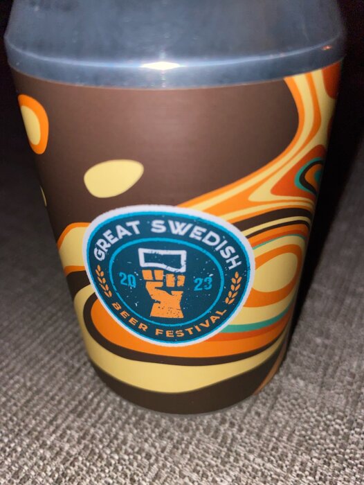 Ett färgglatt termosmugg med "Great Swedish Beer Festival" emblem och årtal 2023, retrodesign, beige och bruna toner.