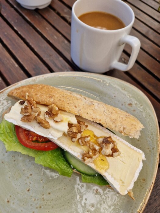 Ett smörgås med brieost, valnötter, sallad, macka på en tallrik, kaffe i bakgrunden.